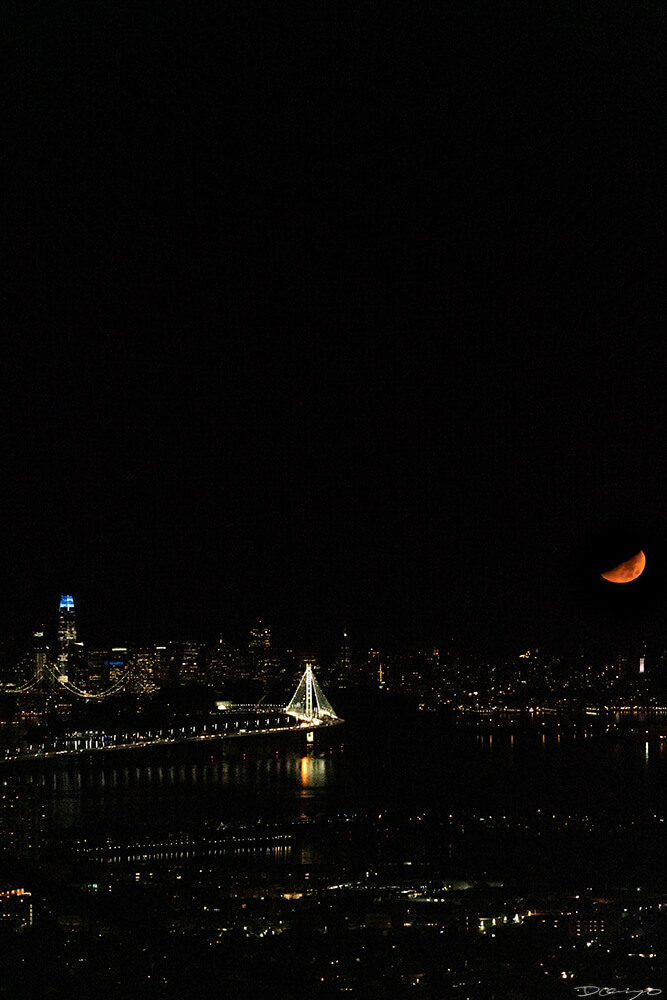 A yellow sliver of the moon sets over the San Francisco Skyline and Bay Bridge, CA