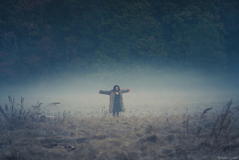 A man in a fur coat spreads his arms in a foggy meadow in Yosemite Valley, CA