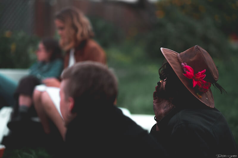 A man wearing a brown hat with a vibrant pink and purple flower in it seen smoking from behind in Berkeley, CA
